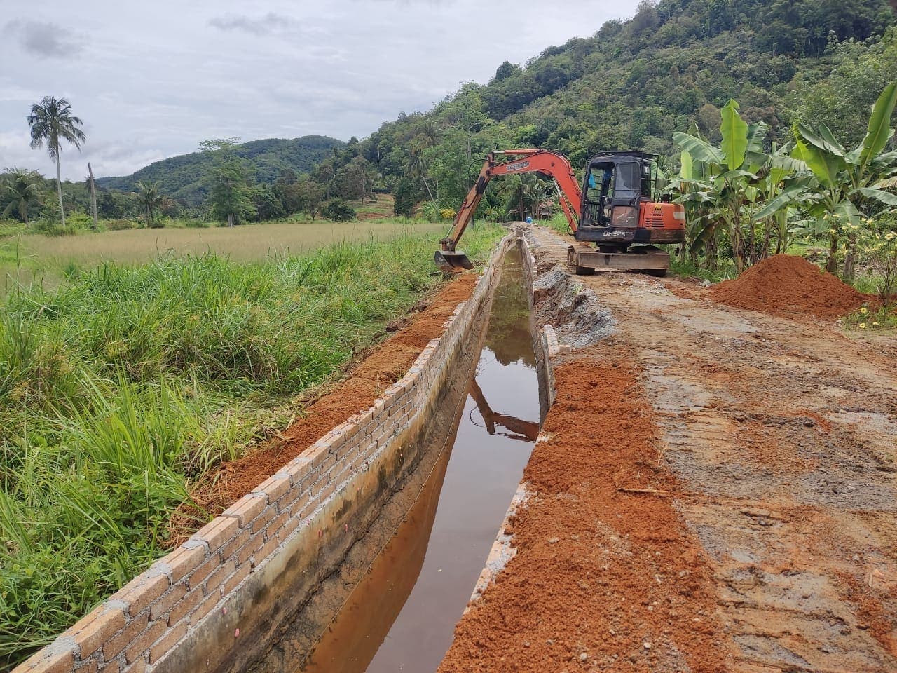 Jentera pengorek menyiapkan parit konkrit di tepi sawah